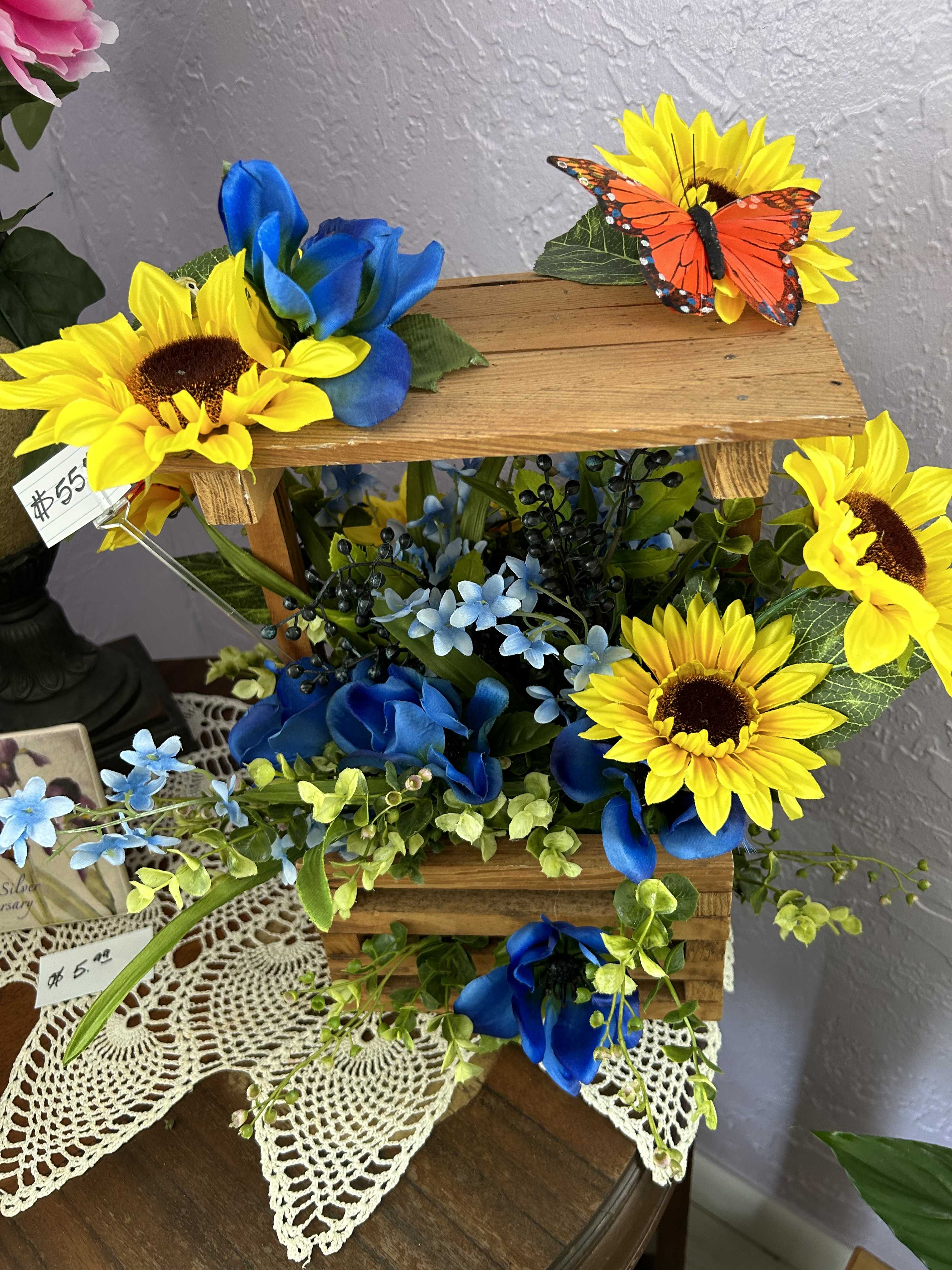 Wooden tiered floral display with sunflowers, blue flowers, and a butterfly