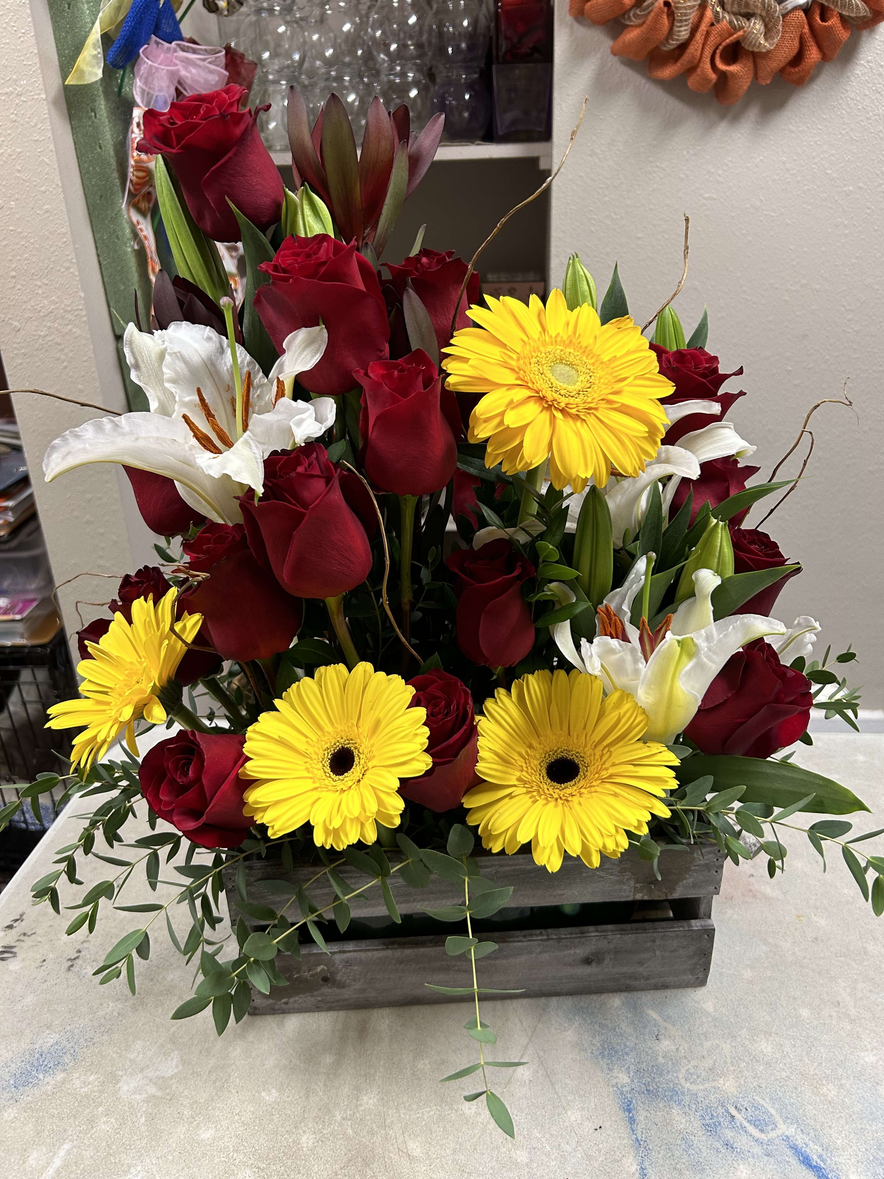 Red roses, white lilies, and yellow gerbera daisies in a wooden box