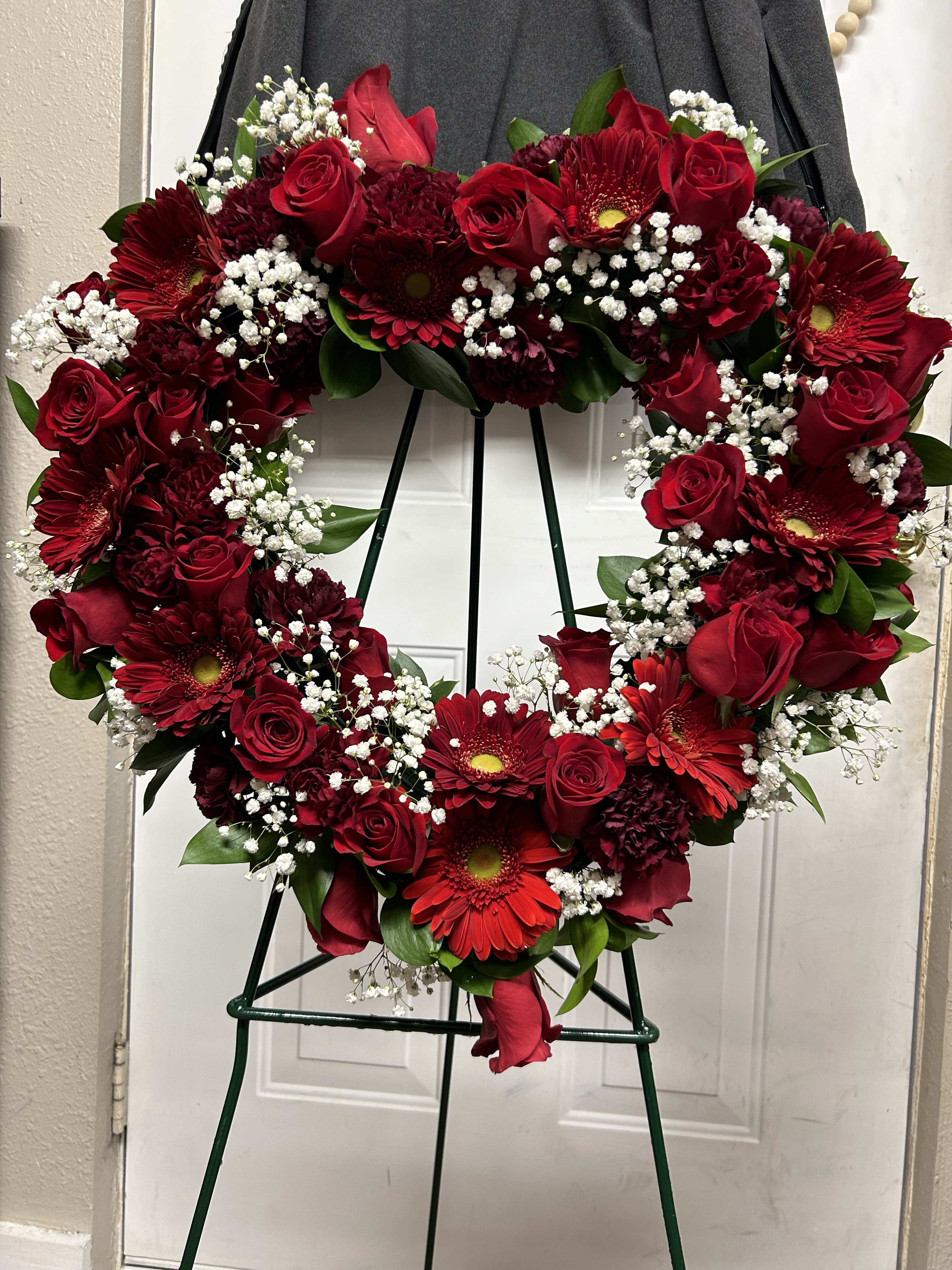Heart-shaped wreath of red roses and gerbera daisies on a stand