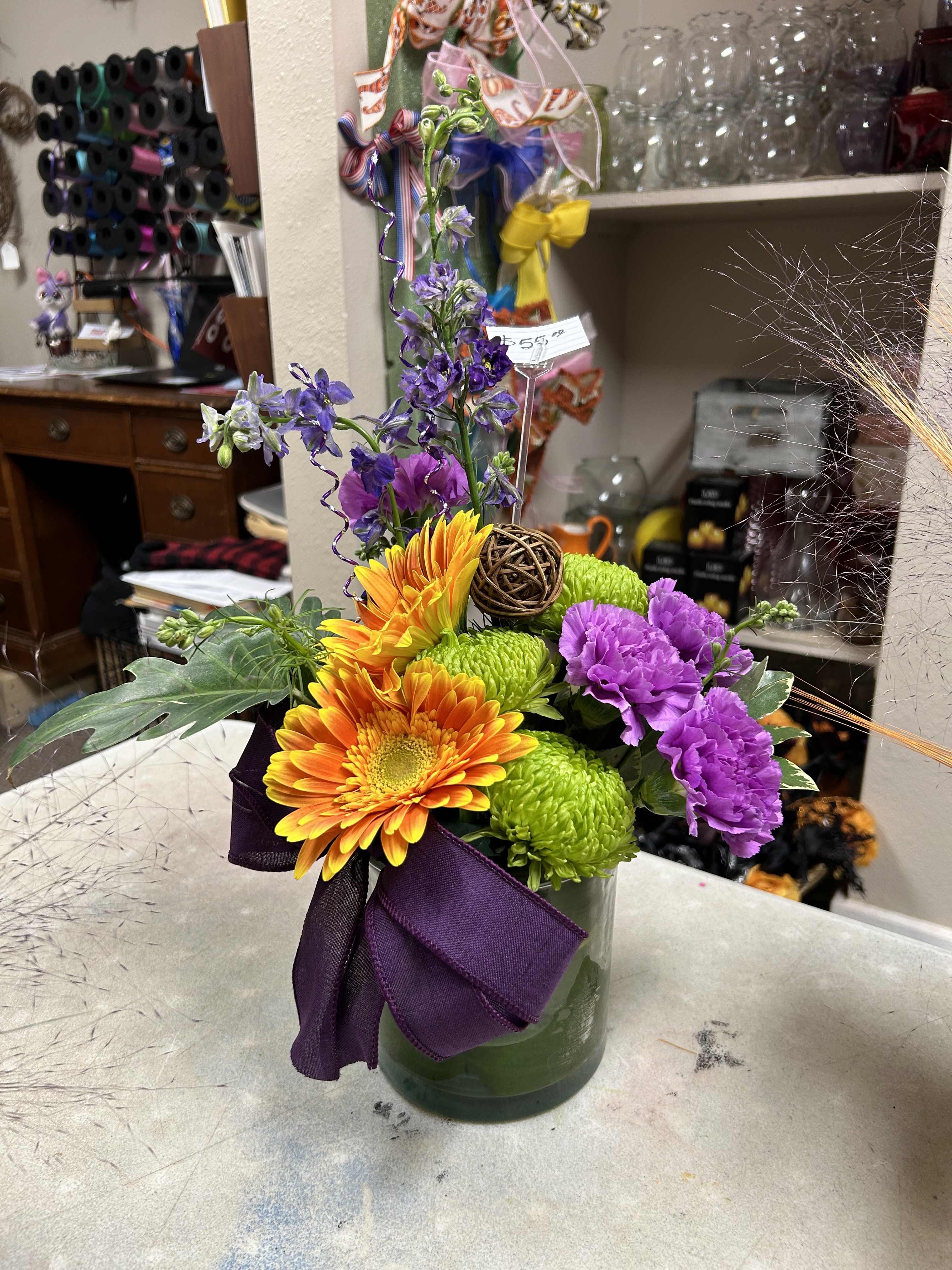 Colorful bouquet in a glass vase with orange gerberas, green mums, and purple carnations