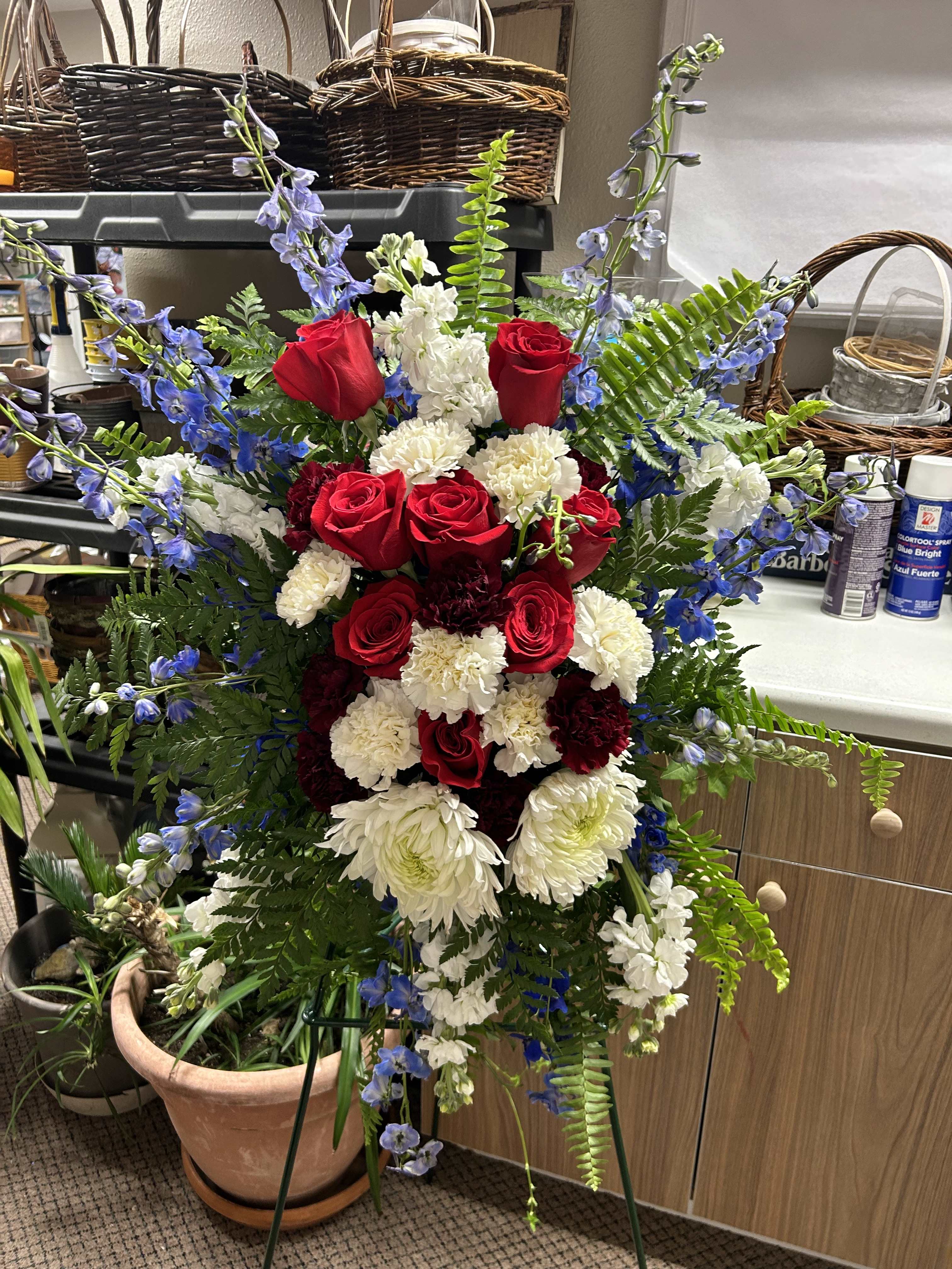 Standing floral spray with red roses, white carnations, and blue delphinium