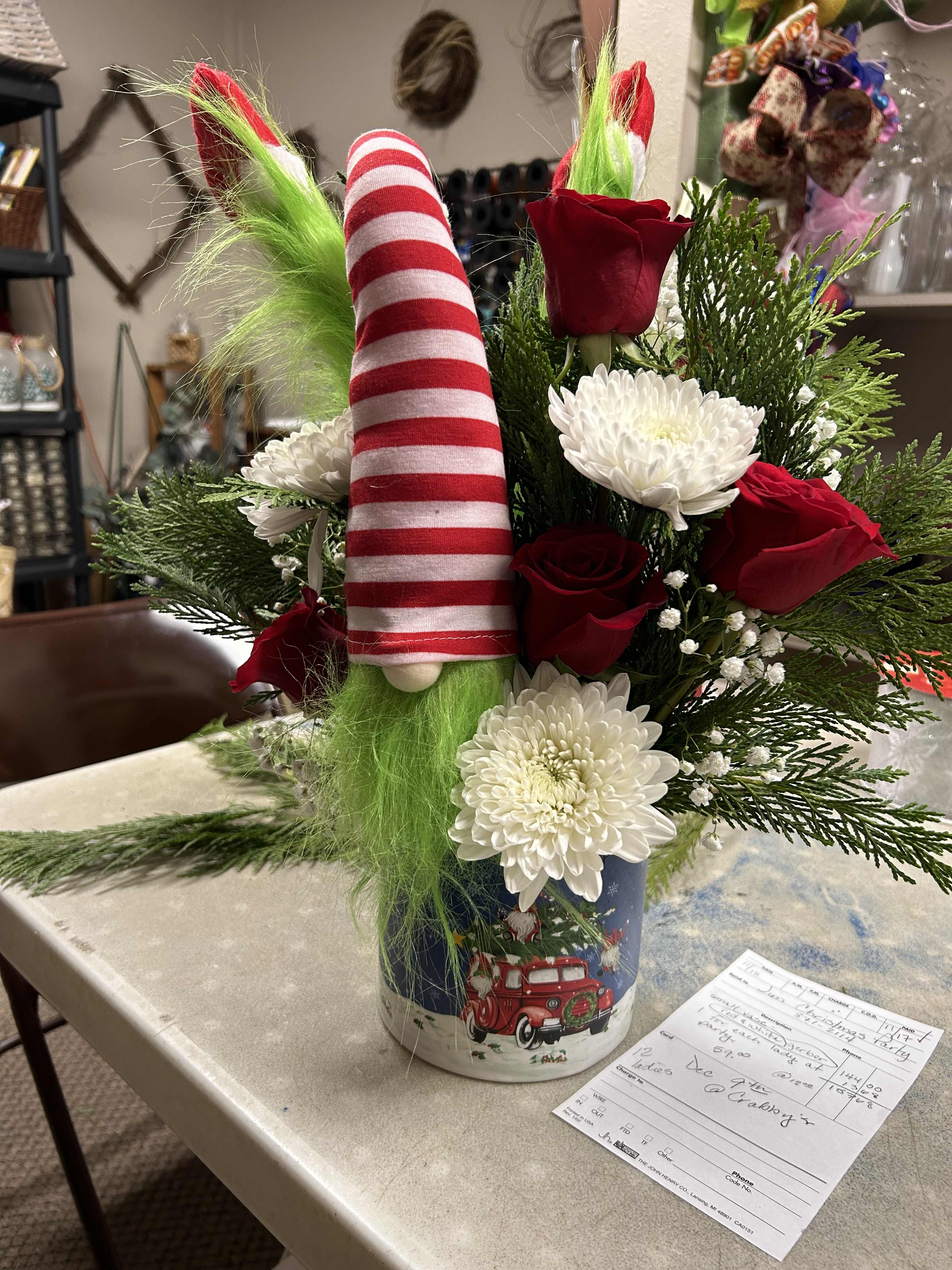 Christmas arrangement with red roses, white mums, and a striped gnome in a holiday tin