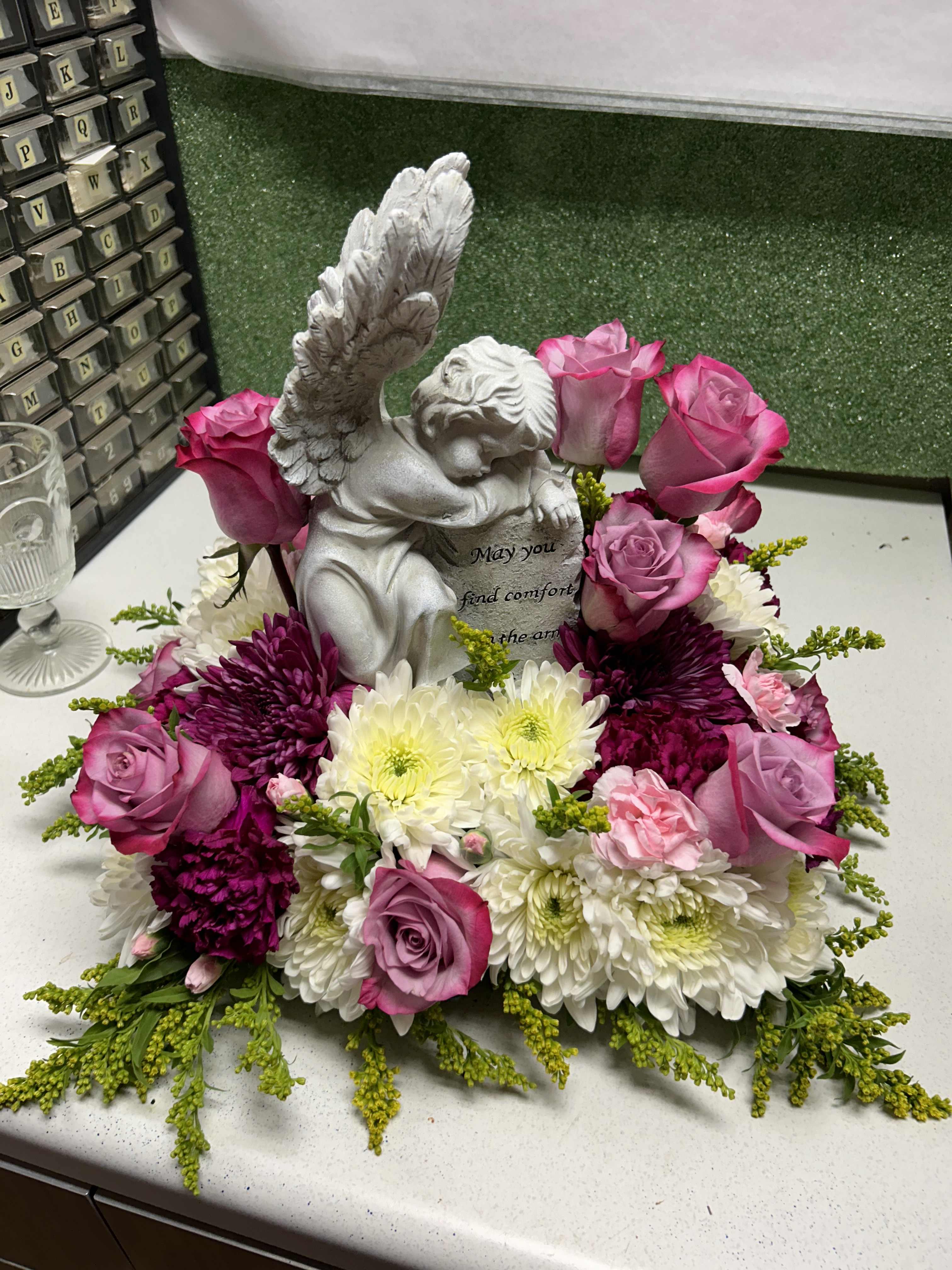 Pink roses and white chrysanthemums arranged around a small angel statue