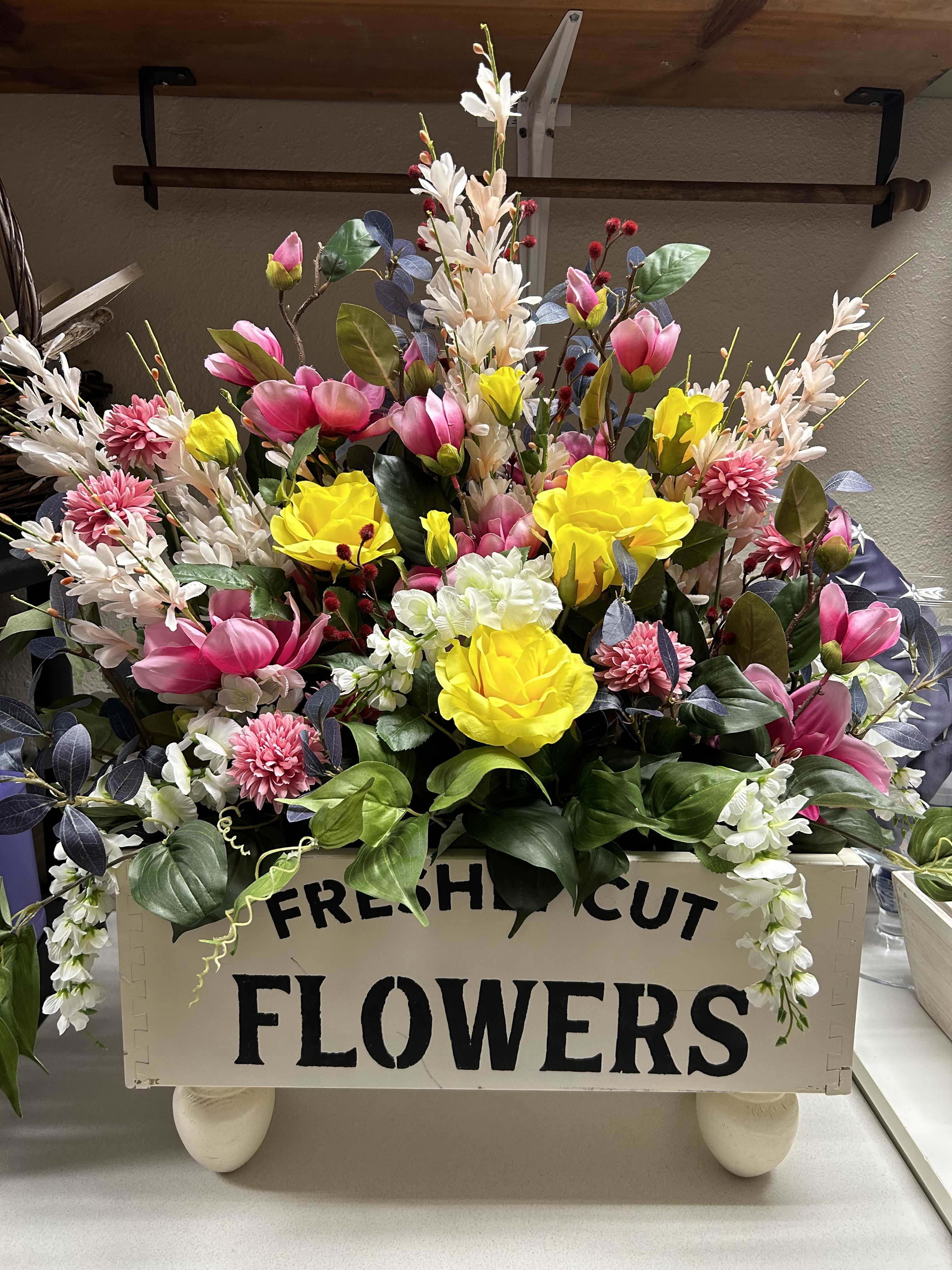 Bright mixed flower arrangement in a wooden box with pink, yellow, and white blooms