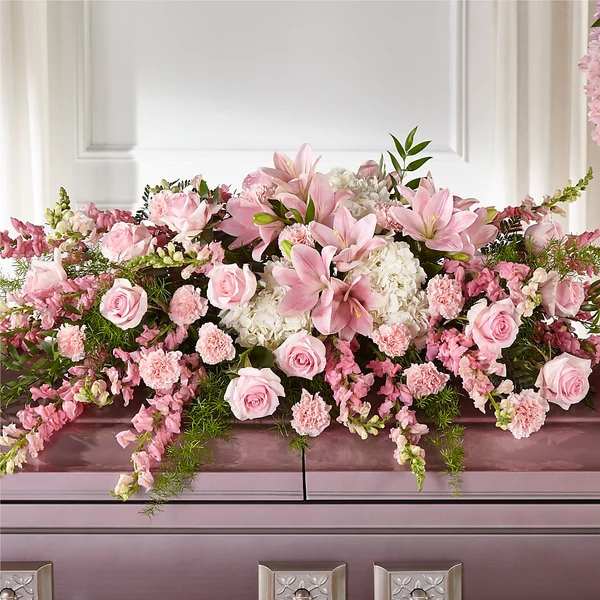 Pink and white floral arrangement with roses and lilies on a casket