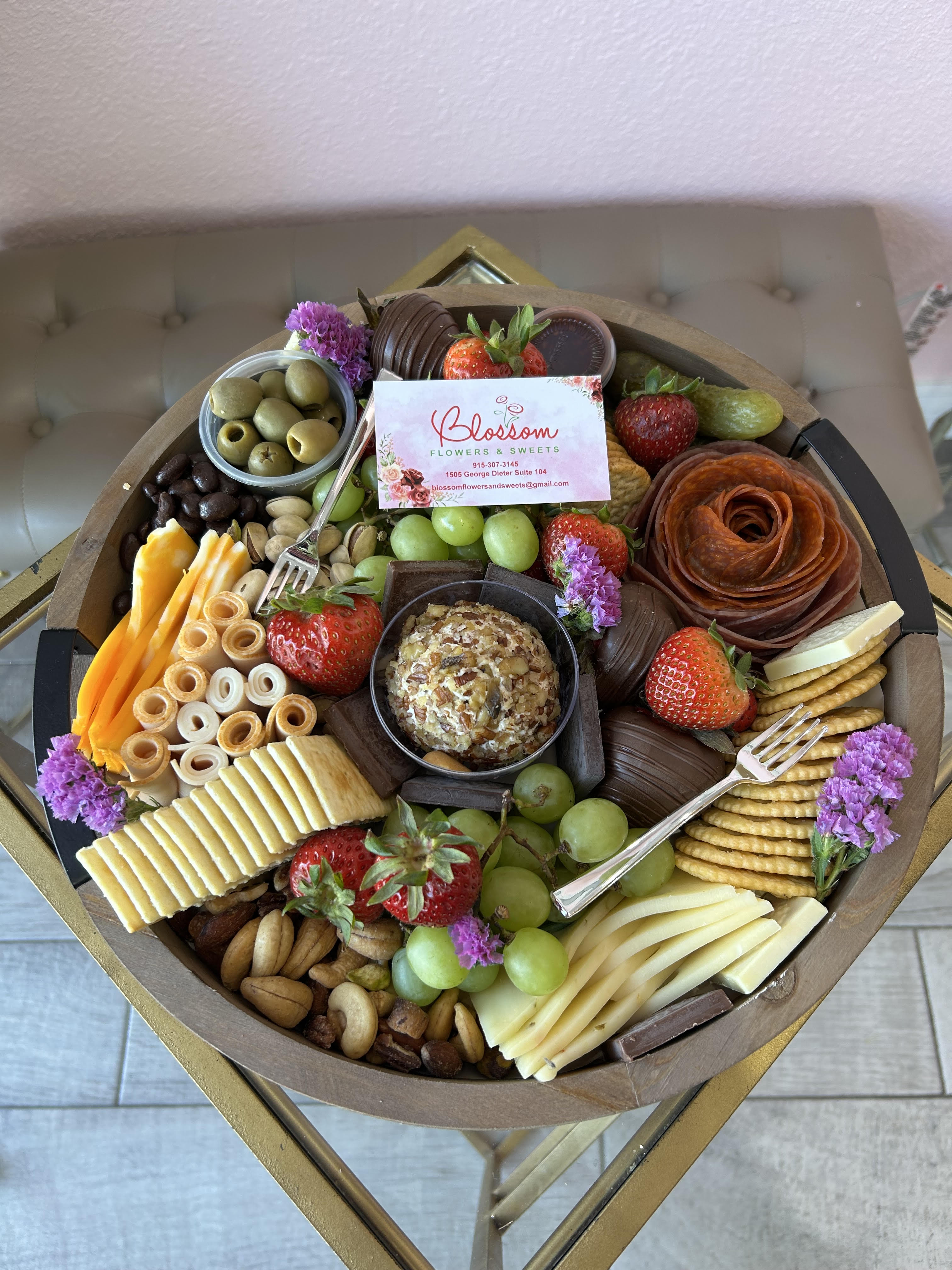 Charcuterie gift tray with fruit, cheese, crackers, nuts, and small purple flowers