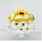 Round floral cake with white daisies and yellow blooms topped by candles