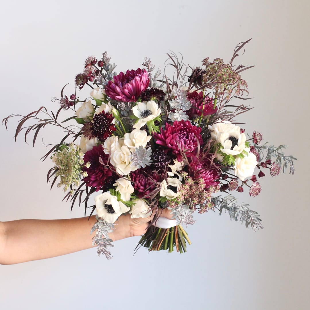 Handheld bouquet of burgundy, white, and pink flowers
