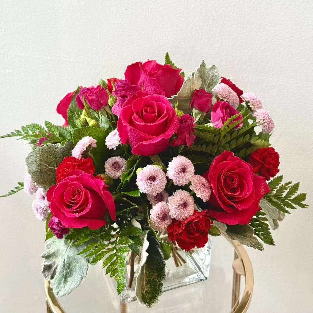 Pink and red rose bouquet with small pale pink blooms in a clear square vase