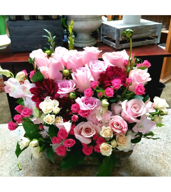 Pink and white rose arrangement with burgundy blooms in a low container