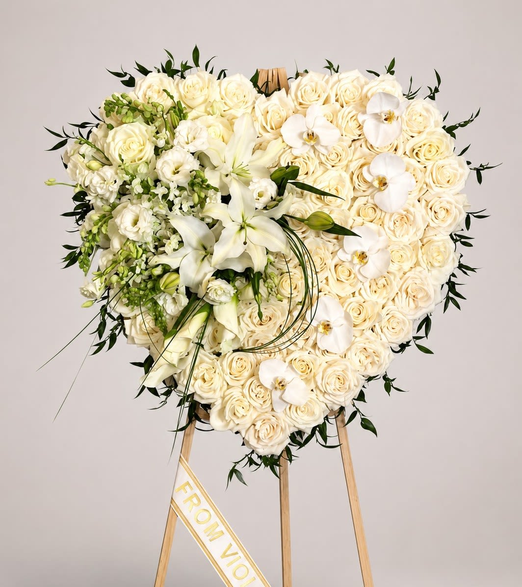 Angelic Heart Memorial - A graceful heart-shaped standing tribute designed with abundant white roses, elegant lilies, orchids, and soft greenery. This timeless arrangement expresses love, peace, sympathy, and remembrance with refined beauty. A printed ribbon or memorial card is included. Please indicate your preference in the “Special Instructions” section at checkout. They can be customized with your message that you can write in the "Card Message" section at checkout. Memorial cards are recommended for longer messages and personal notes while ribbons are best suited for short wording such as names.