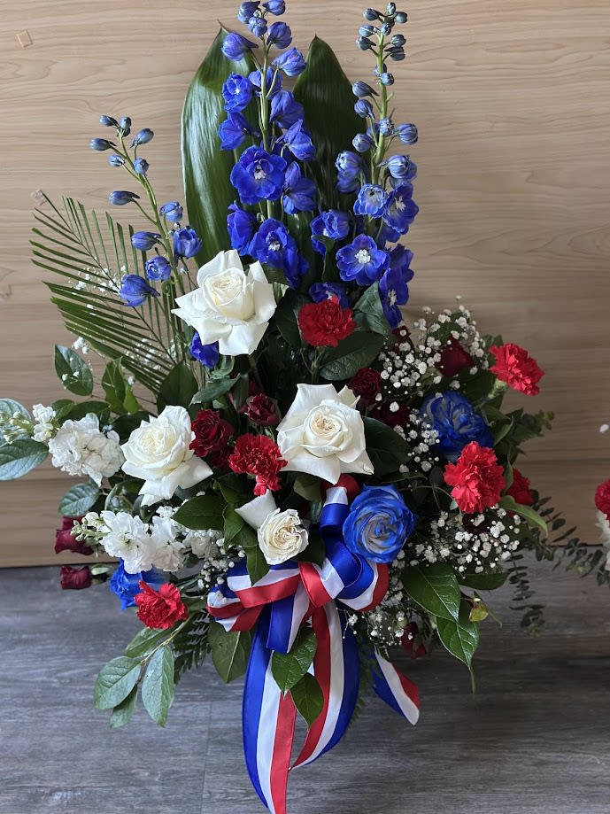 Tall red, white, and blue floral arrangement with roses and blue delphinium