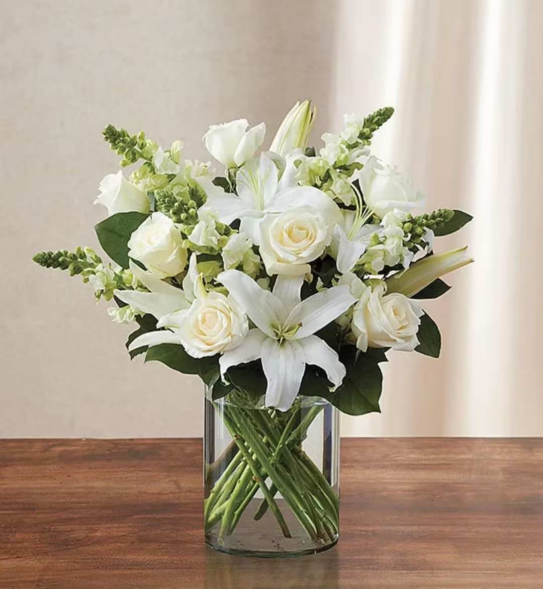 All white Designers choice vase arrangement  - Offer your sincere condolences with our elegant all-white arrangement. Featuring fresh roses, lilies and snapdragons artistically gathered in a clear glass cylinder vase, it will help you express your sympathy straight from the heart.     Our florists hand-design each arrangement, so colors, varieties, and container may vary due to local availability. Lilies may arrive in bud form and will open to full beauty over the next 2-3 days.   Paired with a classic glass cylinder vase; measures 8"H  Large arrangement measures approximately 20"H x 20"L  Medium arrangement measures approximately 19"H x 16"L  Small arrangement measures approximately 18"H x 14"