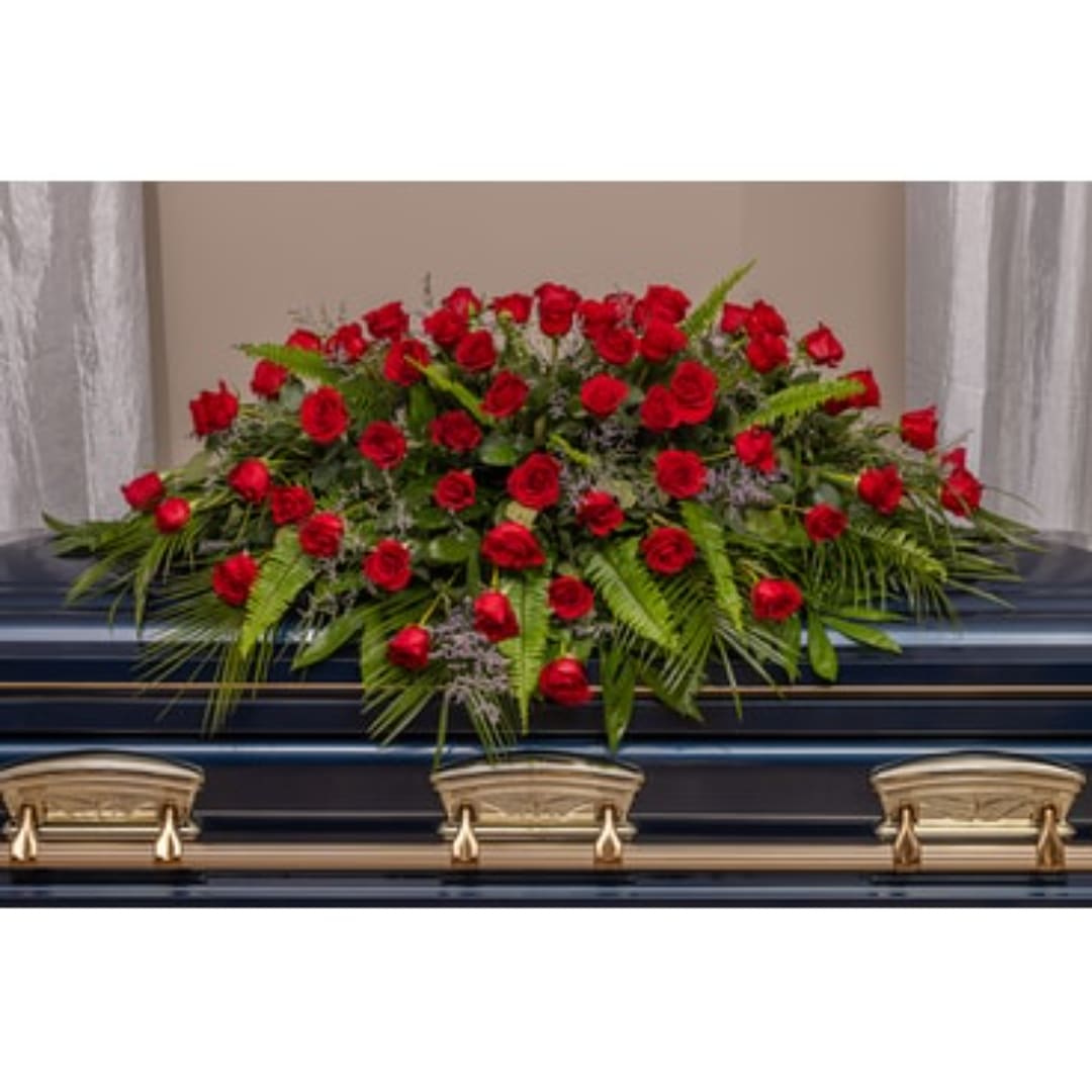 Red rose casket spray with greenery on a dark casket