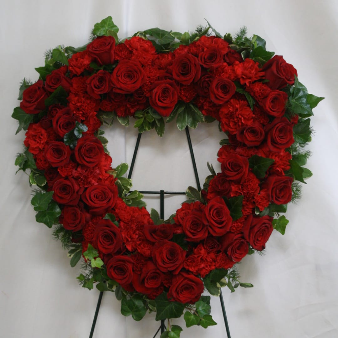 Heart-shaped wreath of red roses with green foliage on a stand