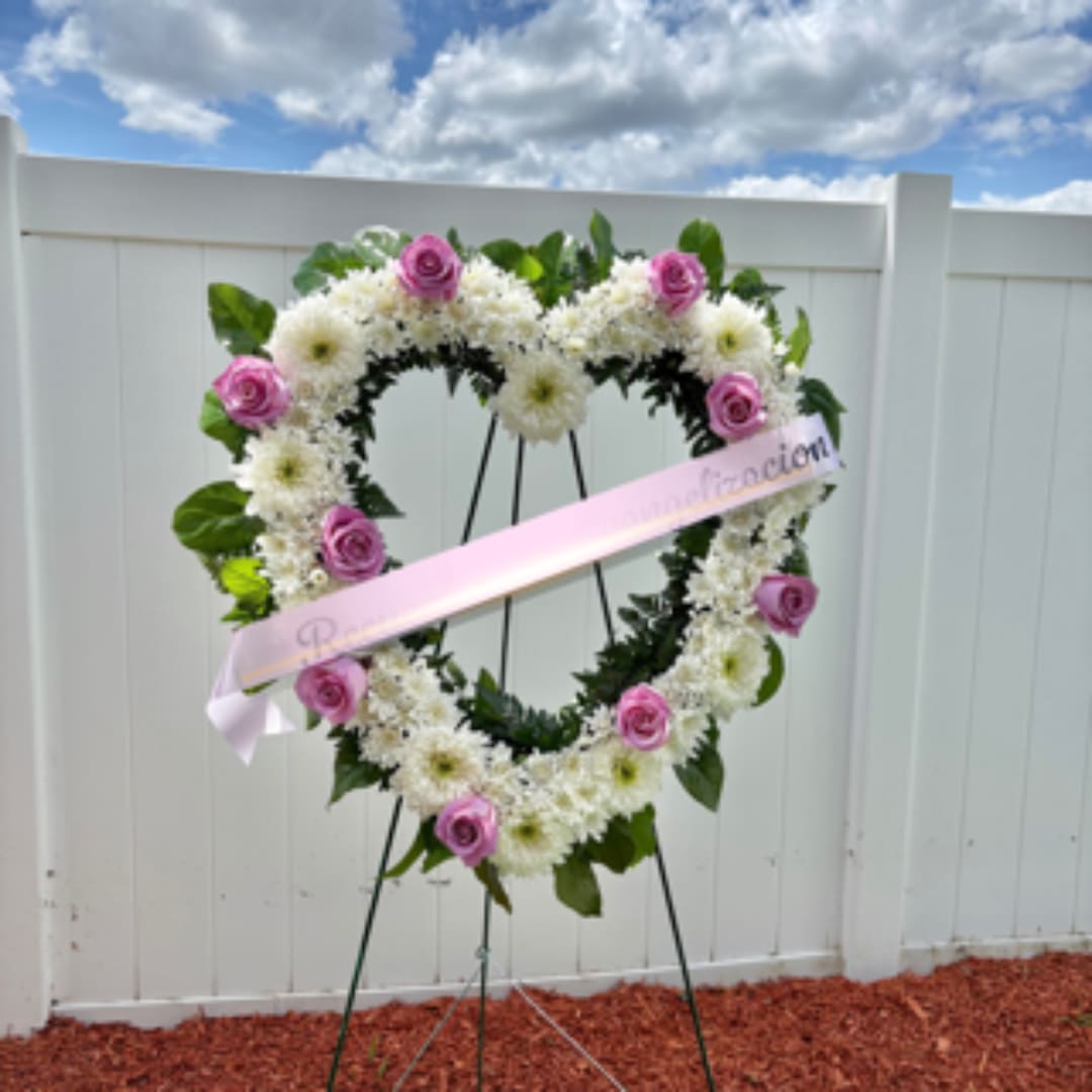 Heart-shaped floral wreath with pink roses and white flowers on an easel