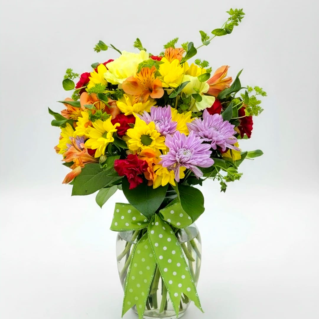 Mixed bouquet of yellow, purple, orange, and red flowers in a glass vase with a green ribbon