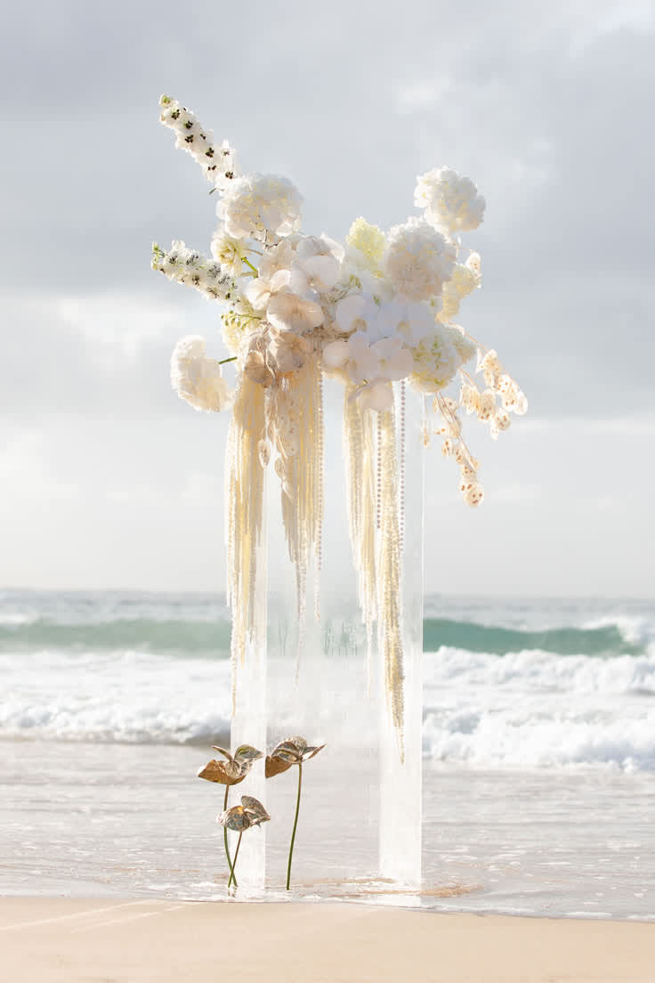 Tall white floral arrangement on a clear pedestal by the beach