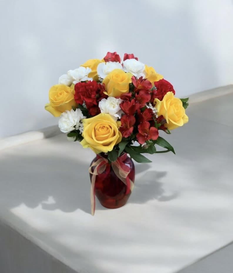 Bouquet of yellow roses, red flowers, and white blooms in a red vase