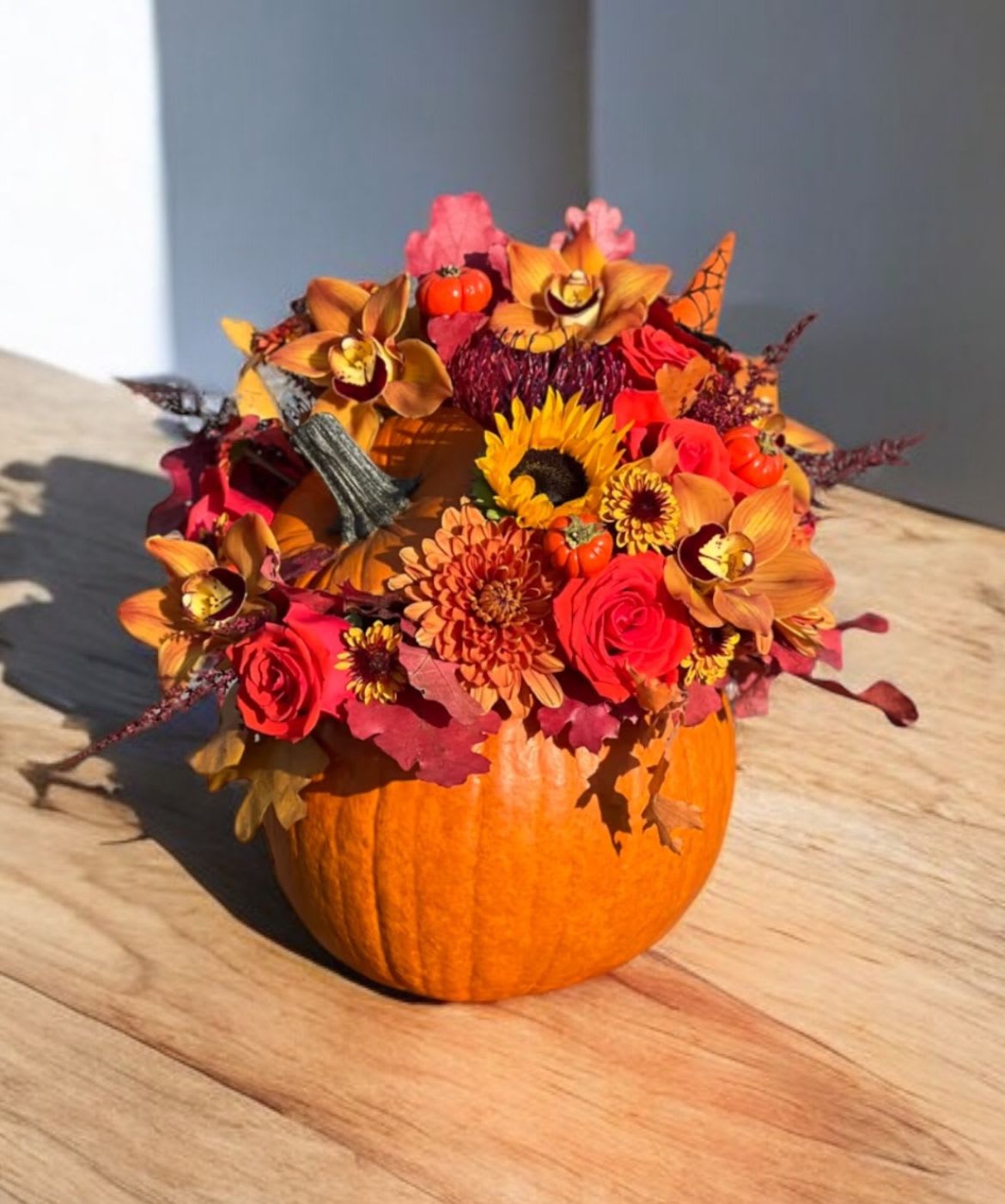 Fall floral arrangement in a pumpkin container with sunflowers and roses