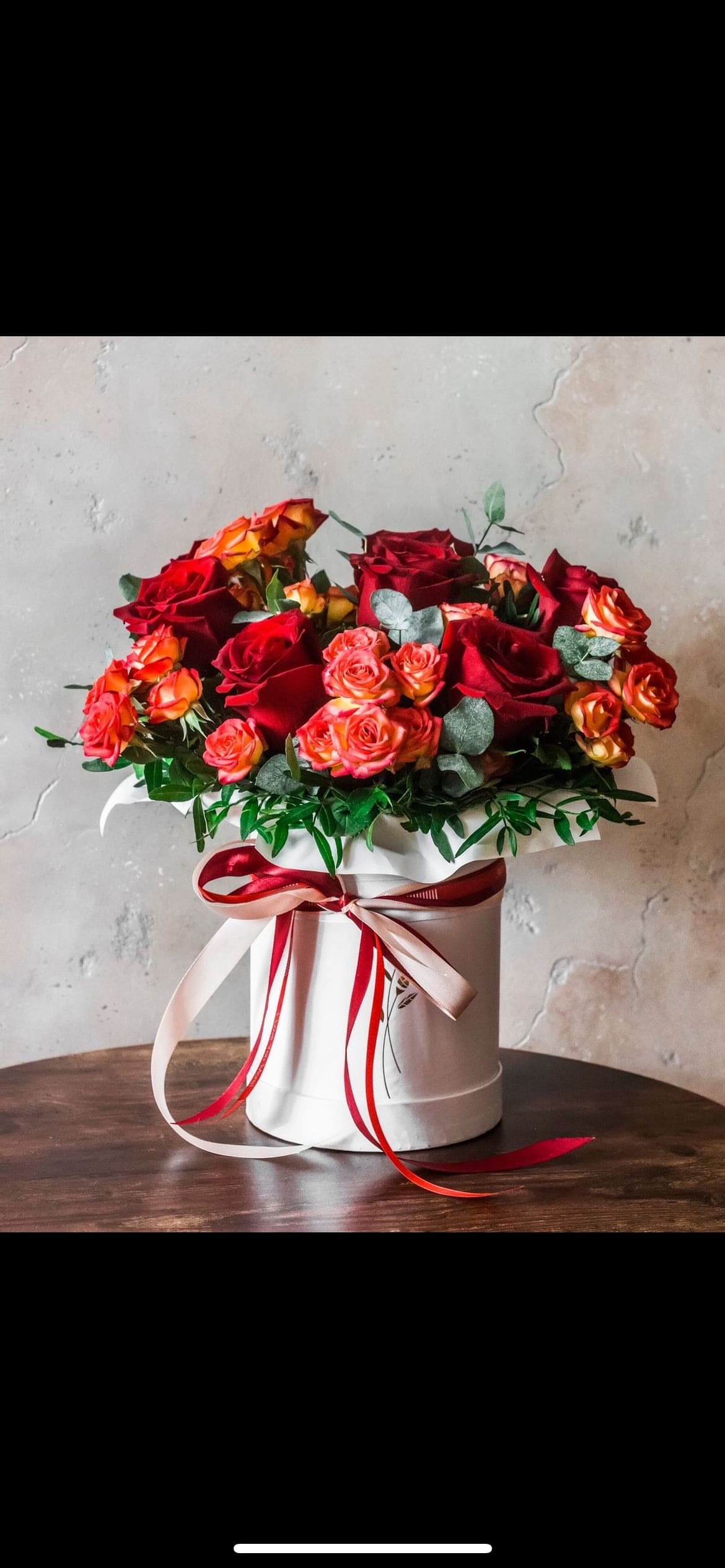 Red and orange roses arranged in a white hatbox with ribbon