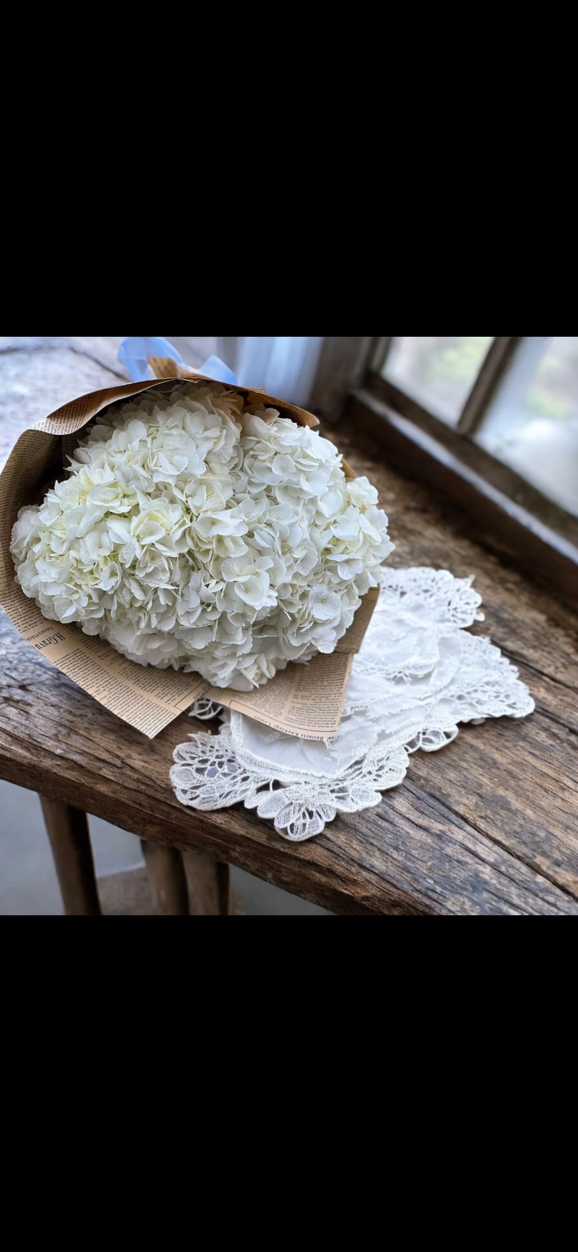 White hydrangea bouquet wrapped in brown paper on a wooden table