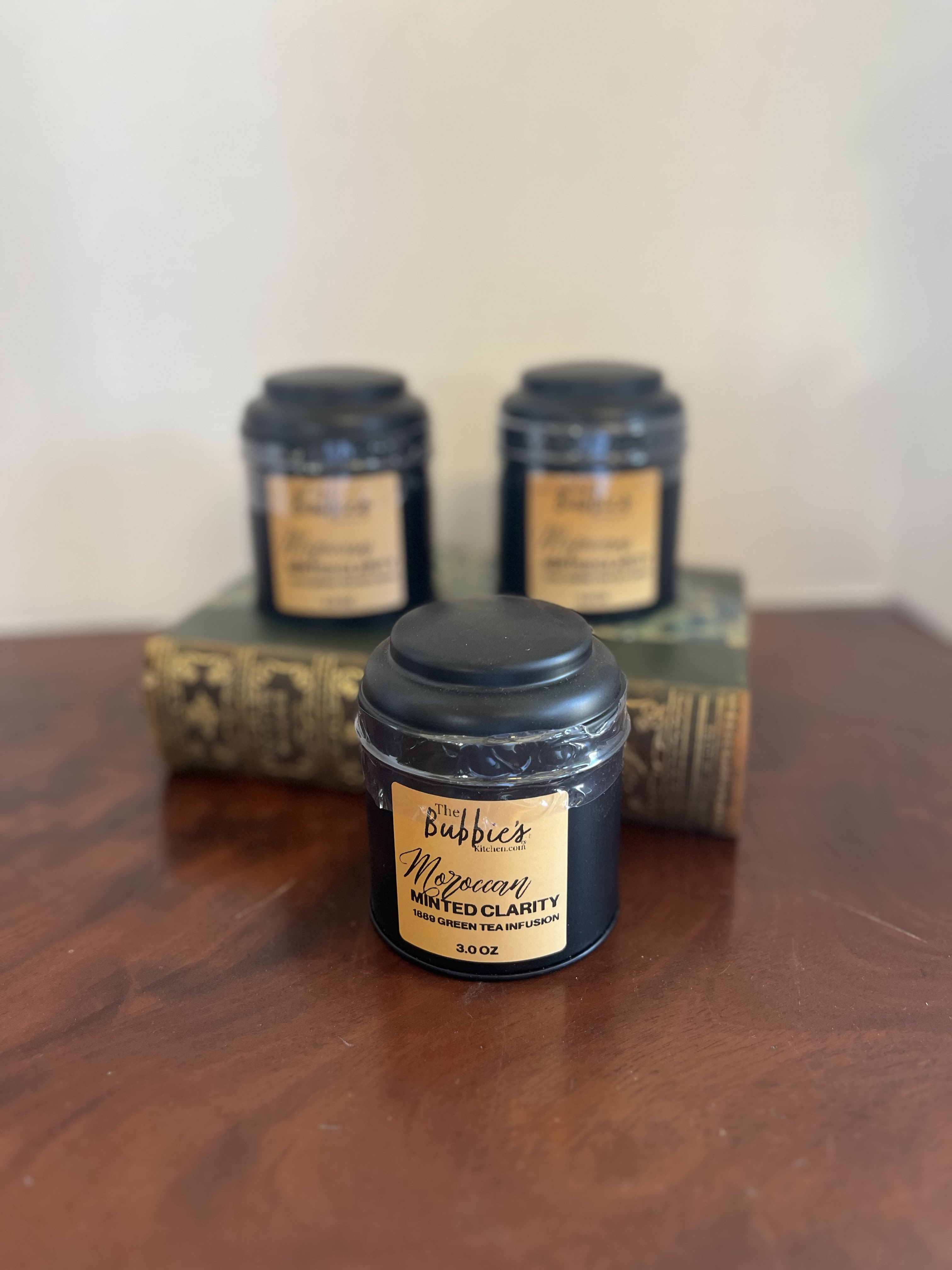 Black tea tin with gold label on a wood surface, with two similar tins blurred behind on stacked books.