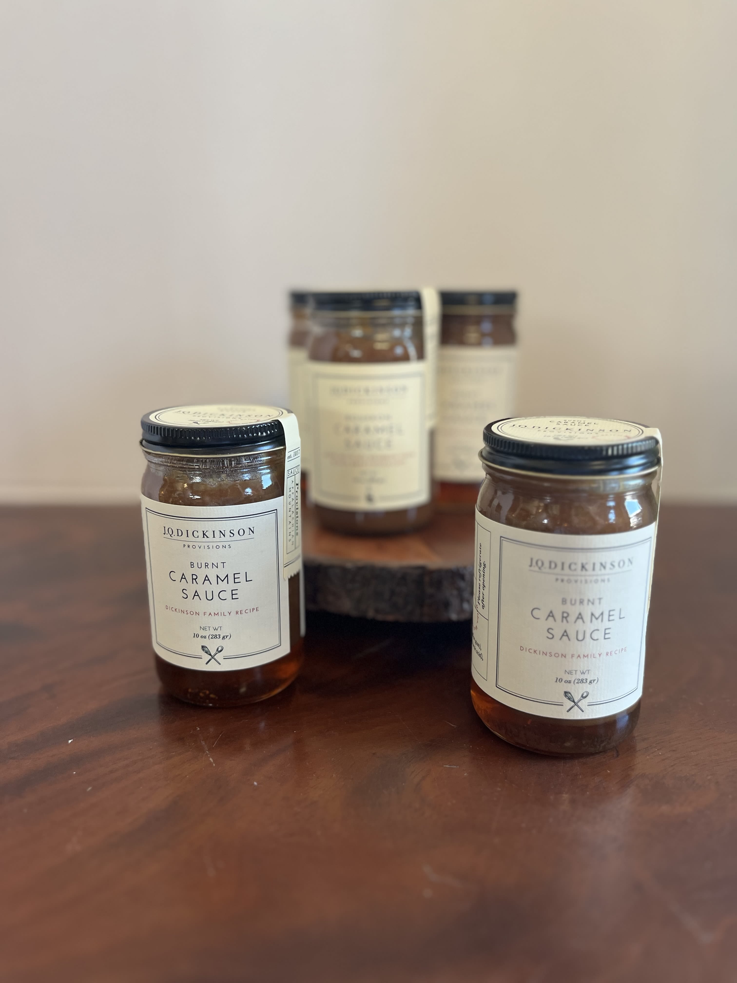 Group of jars of burnt caramel sauce on a wooden surface with one raised on a wood stand