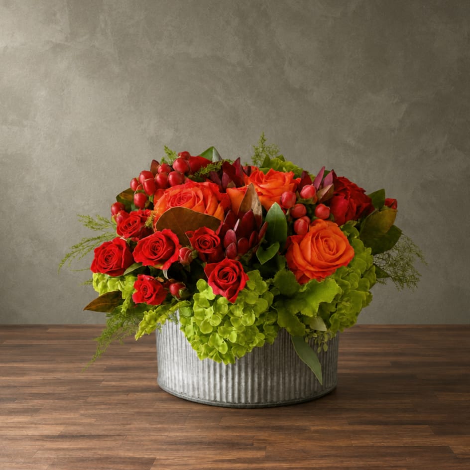 Red and orange roses arranged in a metal container with green hydrangeas
