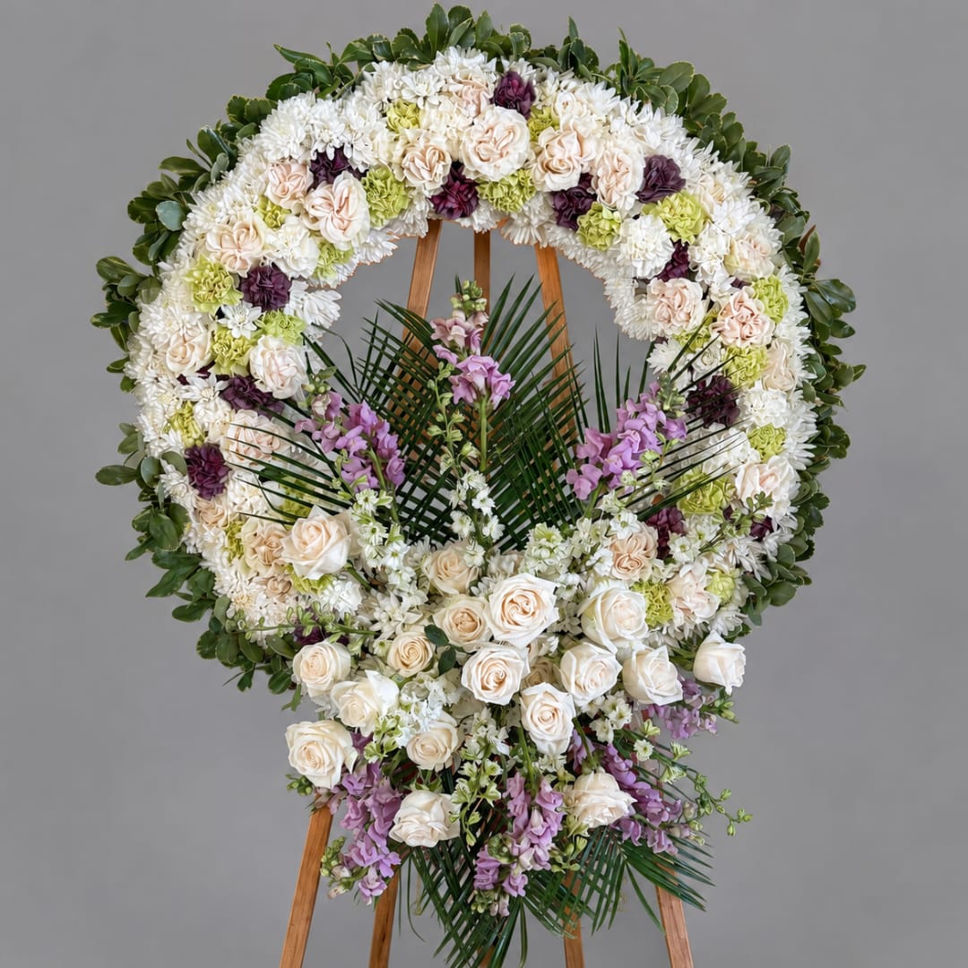 Large floral funeral wreath on a wooden easel with white, cream, purple, and green flowers.
