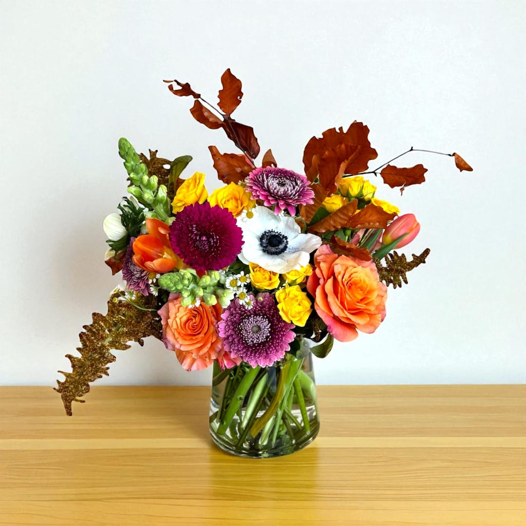 Mixed bouquet of orange, yellow, pink, and white flowers in a glass vase