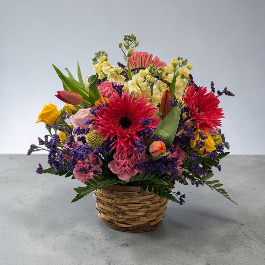 Mixed bouquet in a woven basket with pink, yellow, and red flowers
