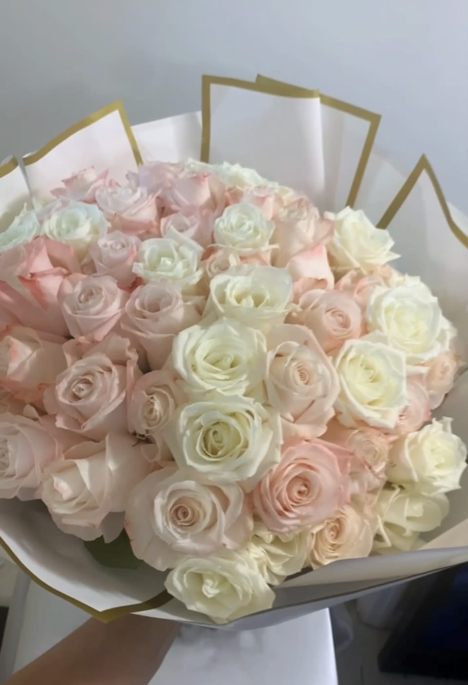 Bouquet of pale pink and white roses wrapped in white paper with gold trim