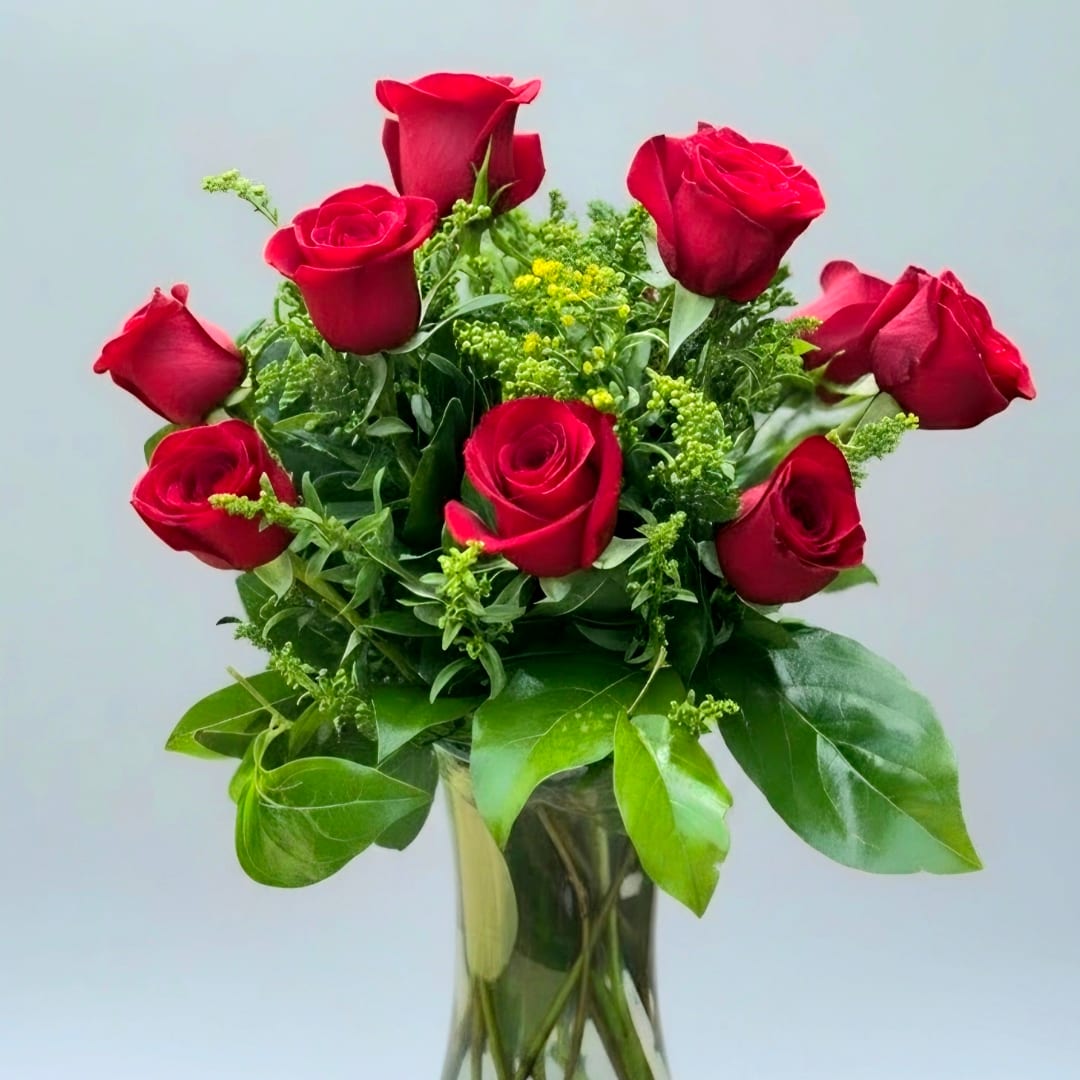Red roses arranged in a clear glass vase with green filler