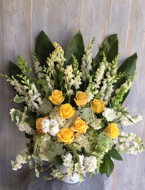Yellow roses and white flowers arranged in a white vase