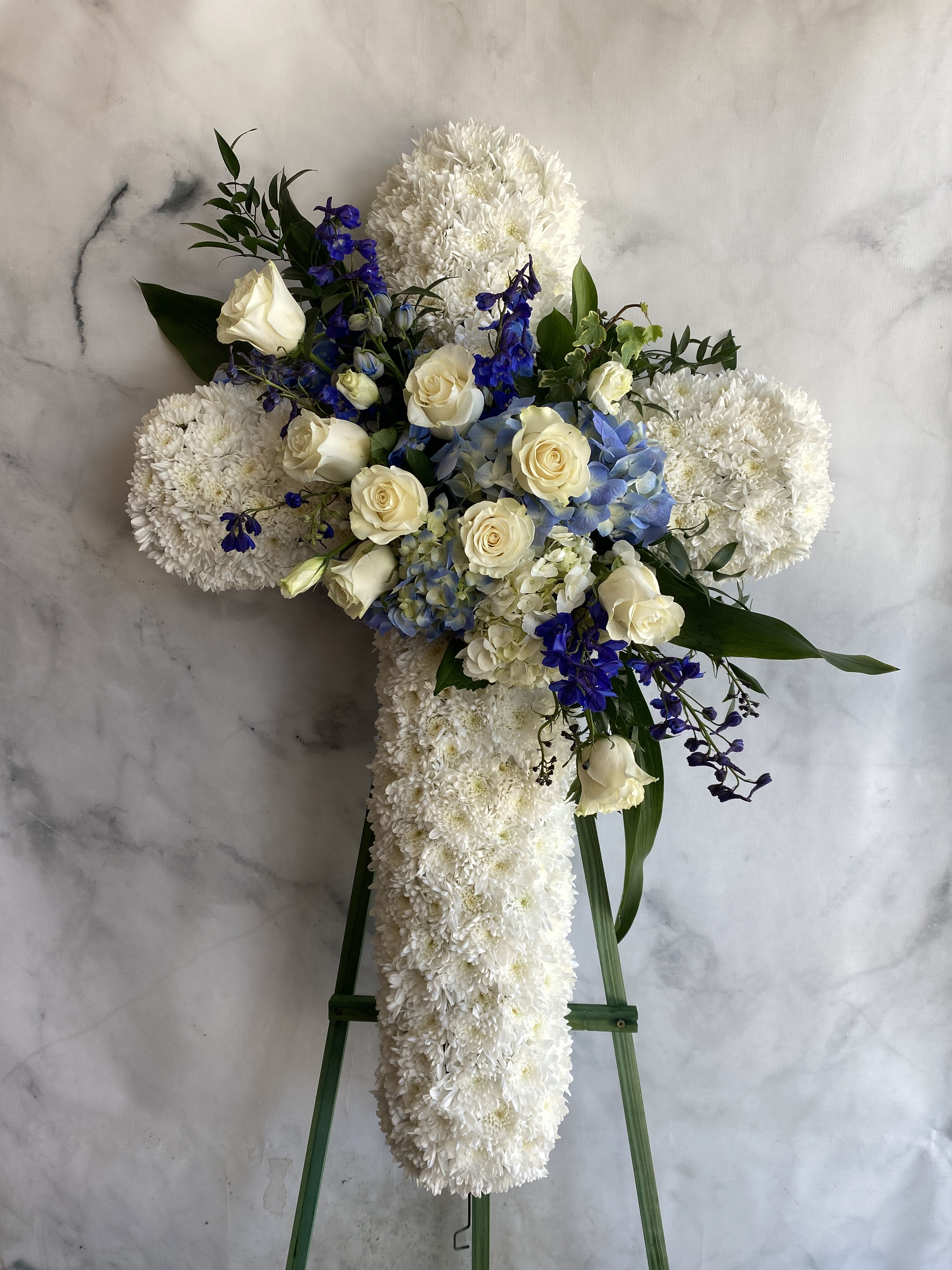 White floral cross on a stand with cream roses and blue flowers