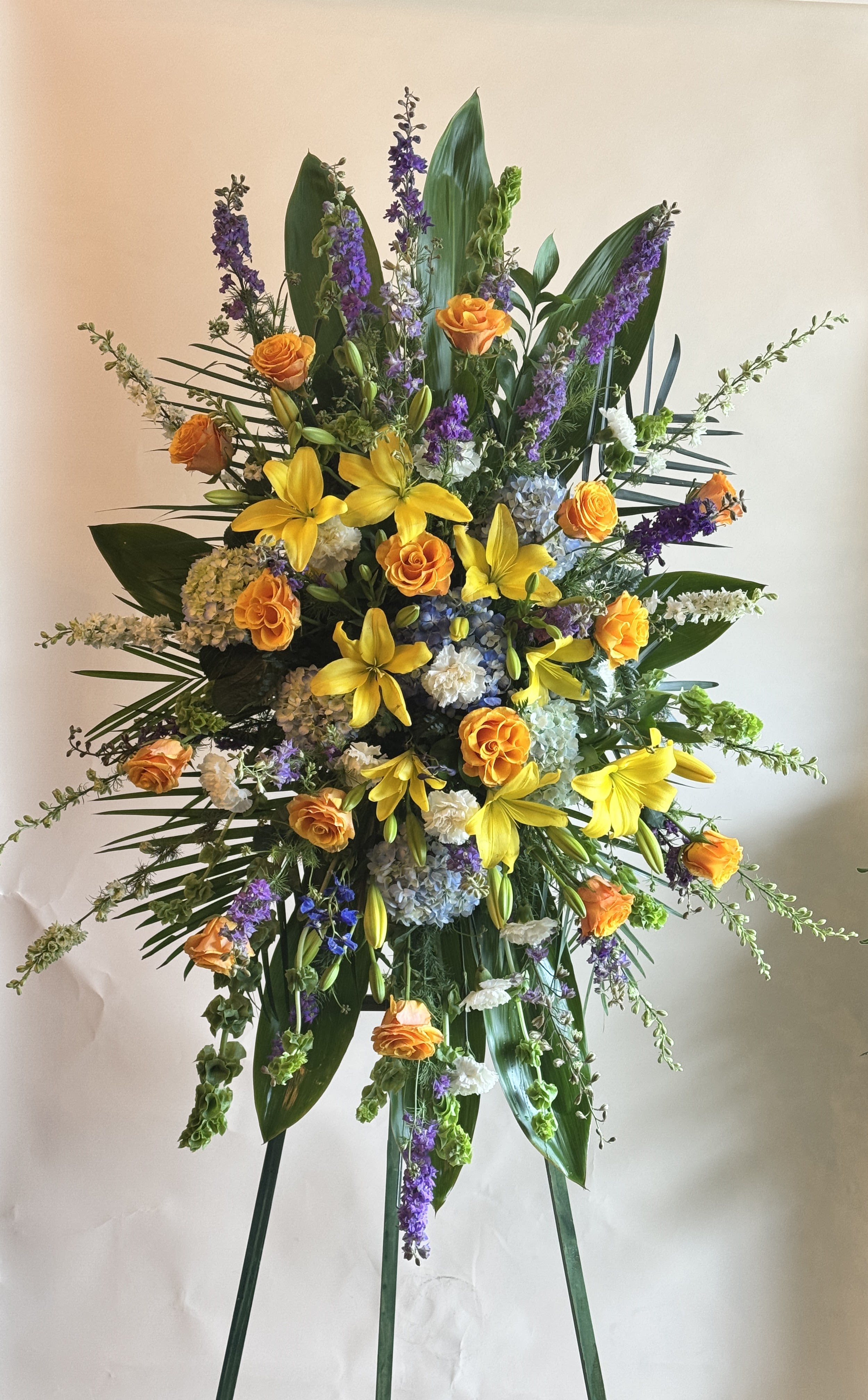 Graceful Spray - A graceful and heartfelt funeral spray featuring a serene blend of lilies, roses, blue hydrangeas, and delphiniums. This arrangement offers a peaceful tribute, combining soft elegance with vibrant blue tones to honor the memory of a loved one with beauty and dignity.