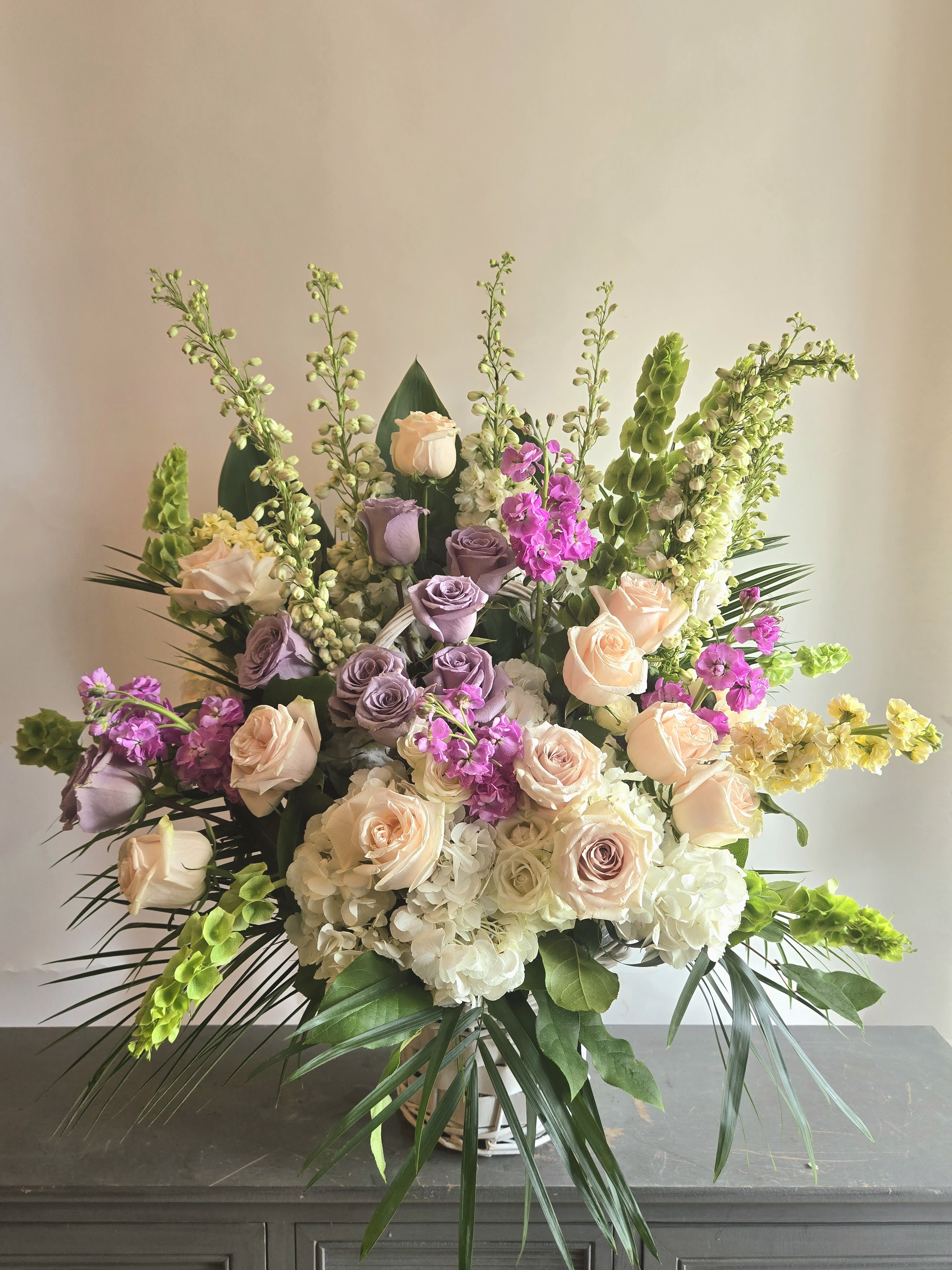 Graceful Beauty - Soothing pastel hues in purple and pink make up this delicate arrangement. Adorned with snapdragons, roses, stock, and hydrangeas. Approximately 3 ft by 2.5 ft.