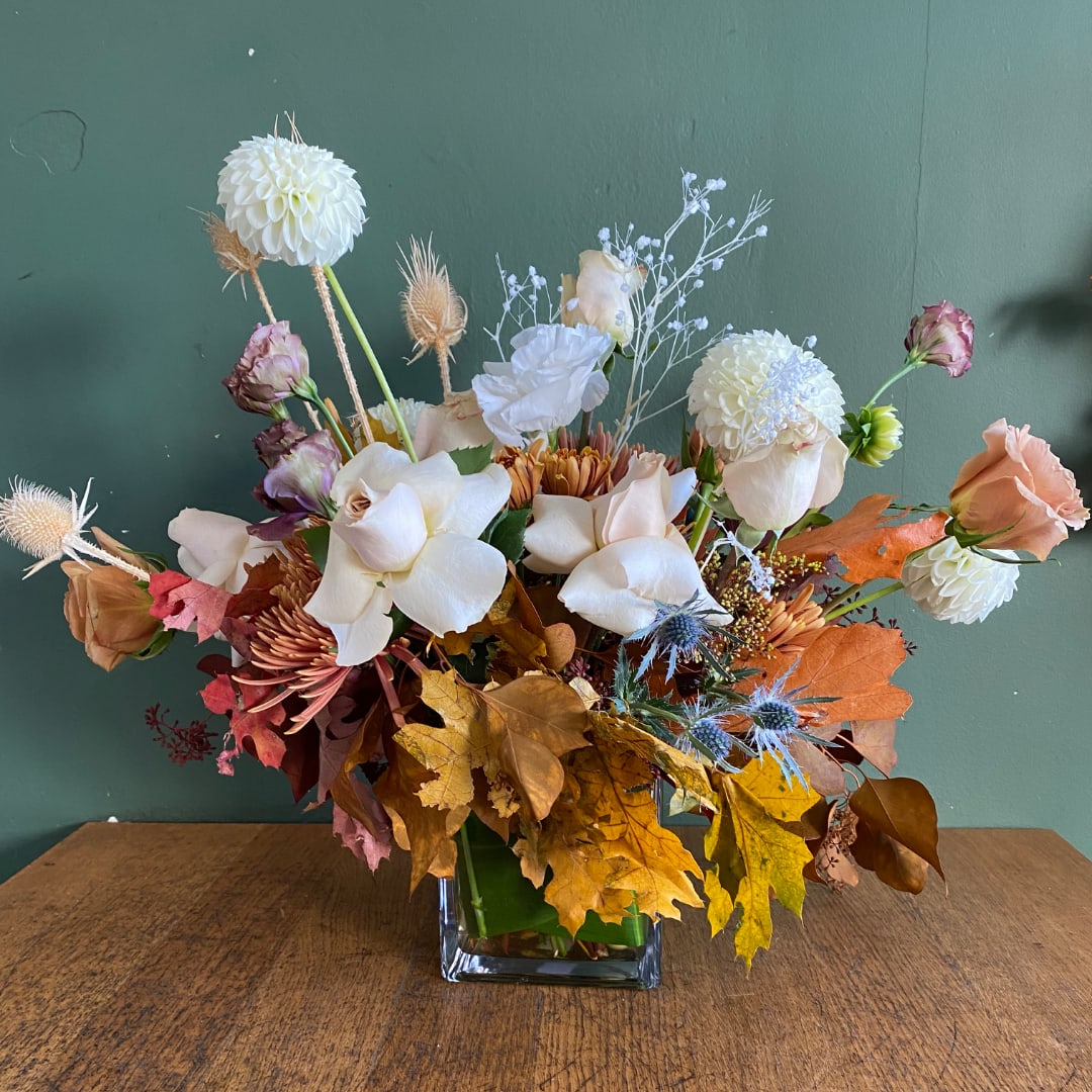 Mixed floral arrangement in a square glass vase with autumn leaves