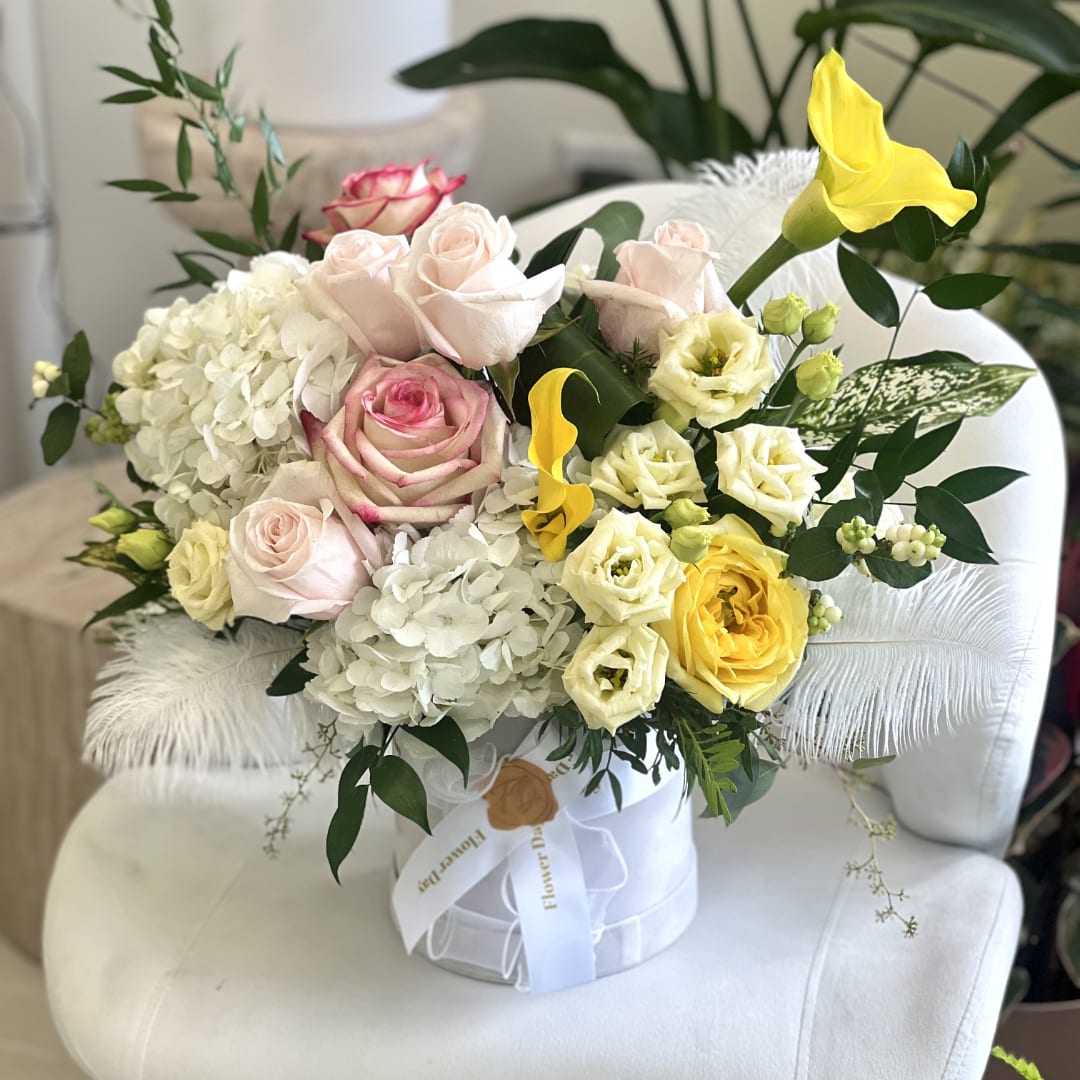 Bouquet of pale roses, white hydrangeas, and yellow calla lilies in a white box