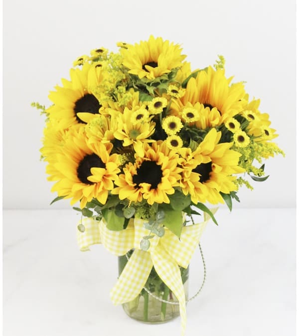 Yellow sunflowers and daisies in a glass vase with a gingham ribbon