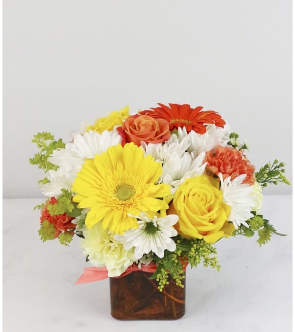 Bright mixed flower arrangement in a square glass vase