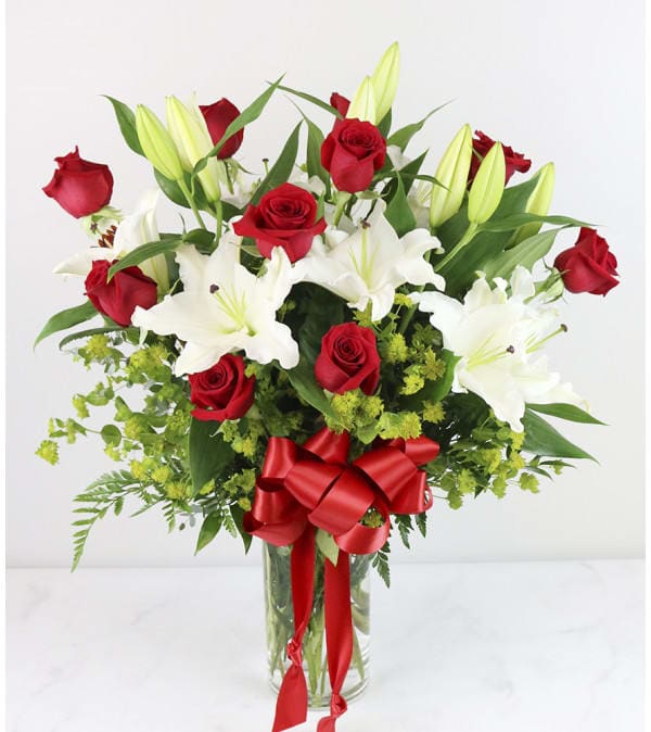 Bouquet of red roses and white lilies in a glass vase with a red ribbon