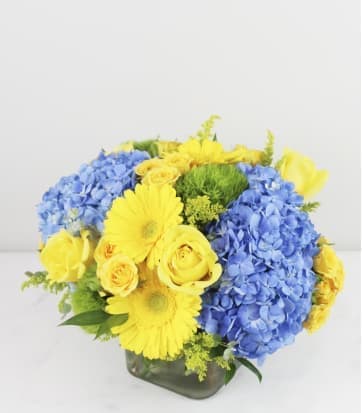 Blue hydrangeas and yellow roses in a square glass vase