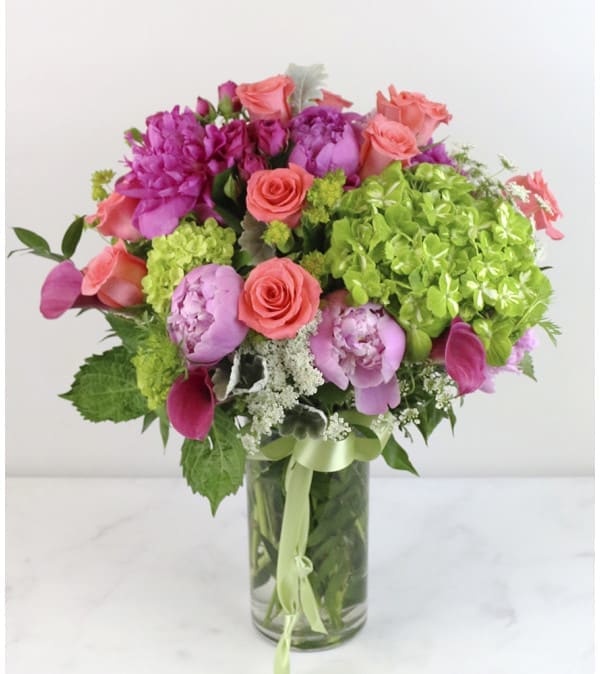 Bouquet of pink and coral flowers in a clear glass vase with a green ribbon