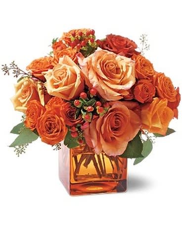 Orange and peach roses arranged in a square amber vase