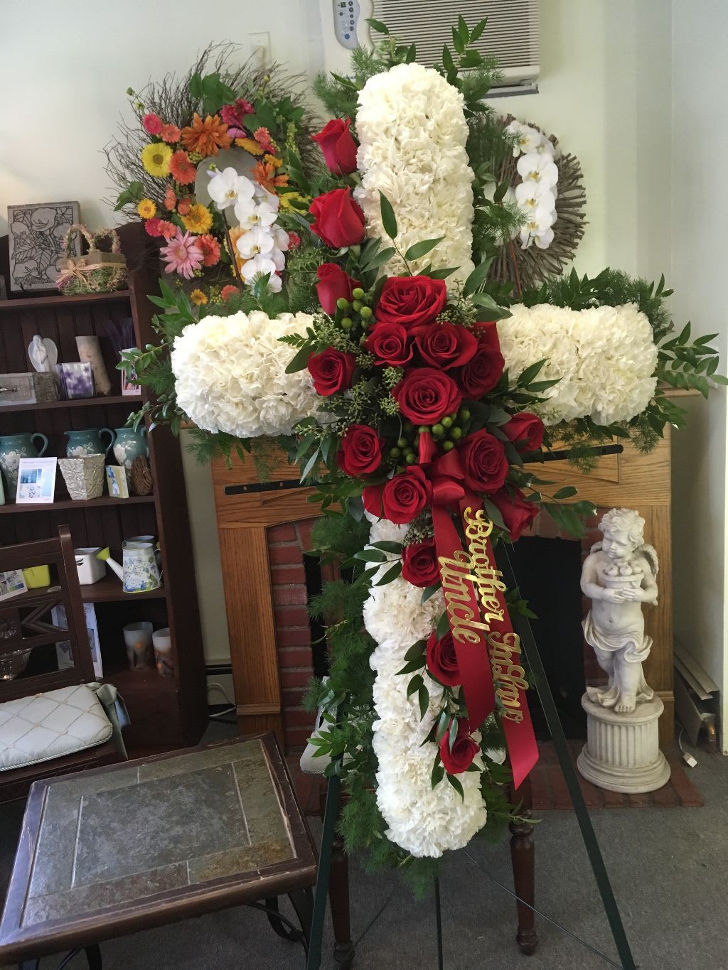 Large funeral cross of white flowers and red roses with a ribbon