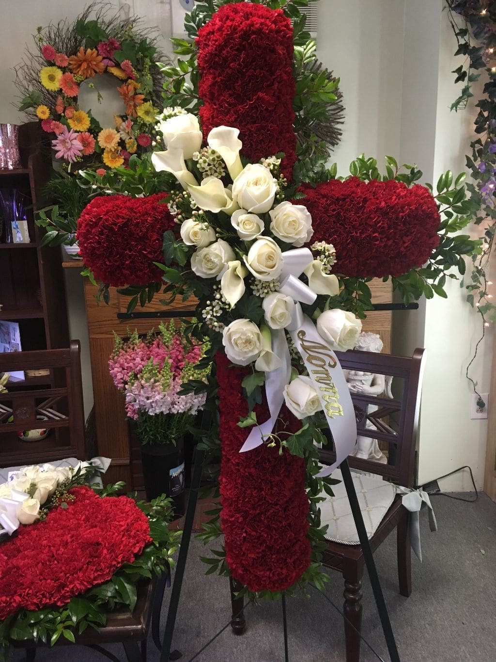 Large red floral cross with white roses and calla lilies on an easel