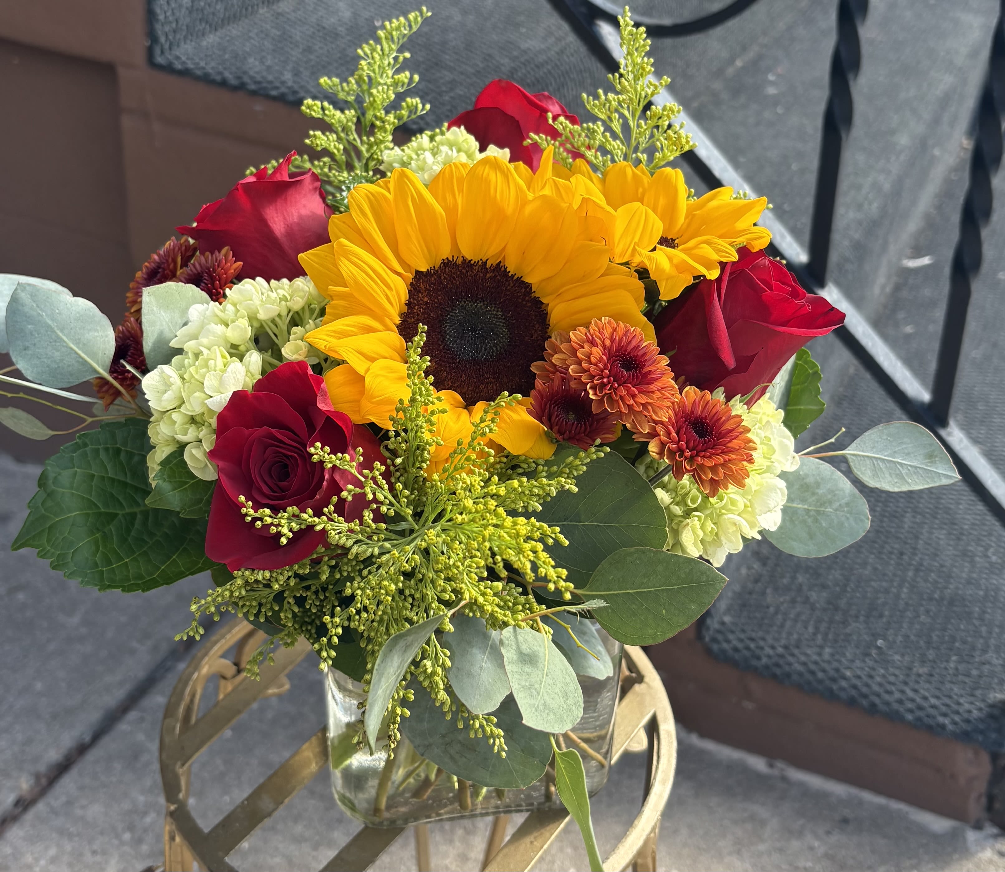 Bouquet with a sunflower, red roses, and orange mums in a glass vase