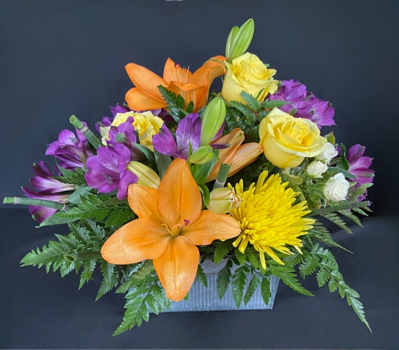 Orange lilies, yellow roses, and purple alstroemeria in a rectangular vase